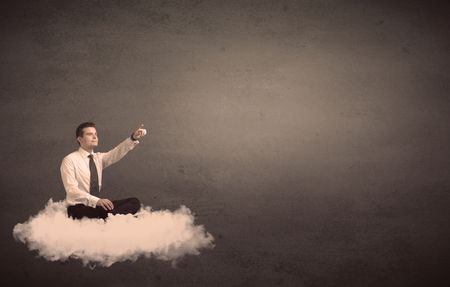 Caucasian businessman sitting on a white fluffy cloud wondering with a plain grunge background