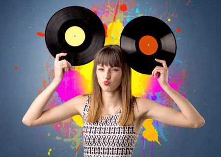 Young lady holding vinyl record on a grey background with colorful splashes behind her