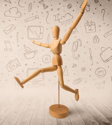 Wooden mannequin posed in front of a greyish background with mixed media scribbles behind it