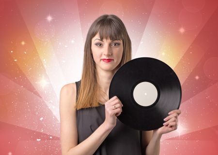 Young lady holding vinyl record on a red background with lights shining behind her