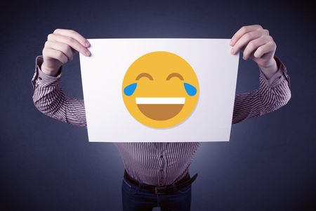 Young businessman hiding behind a laughing emoticon on cardboard