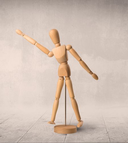 Wooden mannequin posed in front of a greyish background