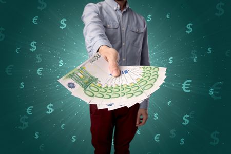 Young businessman holding large amount of bills with green background and currency symbols 