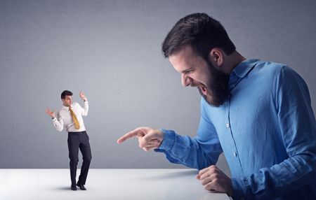 Young professional businessman being angry with an other miniature businessman in front of a grey background