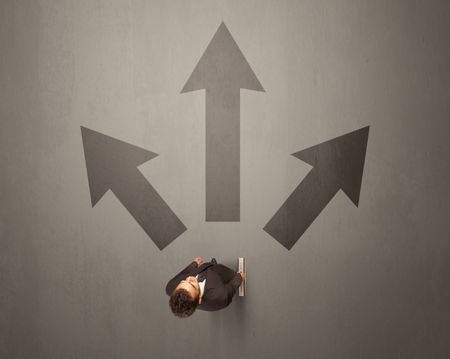 Young contemplating businessman stands in front of brown arrows