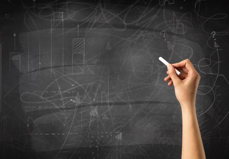 Female hand holding white chalk in front of a blackboard with scribbles and plans drawn on it