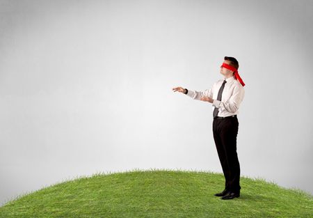 Young blindfolded businessman steps on a patch of grass