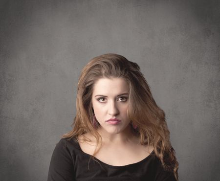 pretty-young-teenage-girl-standing-front-608795435 A pretty young teenage girl standing in front of a grey clear empty urban wall background concept while making funny faces.