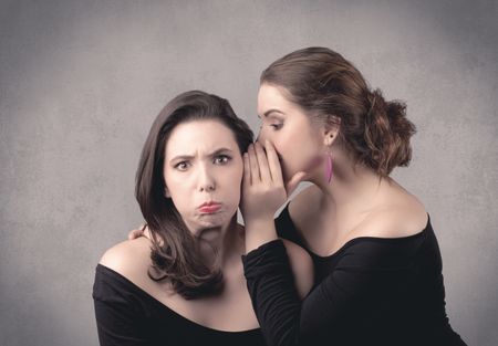 Two fancy dressed actress girls with long hair and make up whispering in front of grey urban background concept.