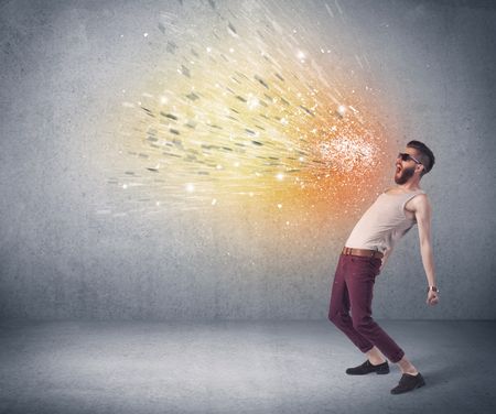 A young hipster guy with beard and sunglasses shouting in front of urban wall with vomit like colorful paint splatter on wall concept