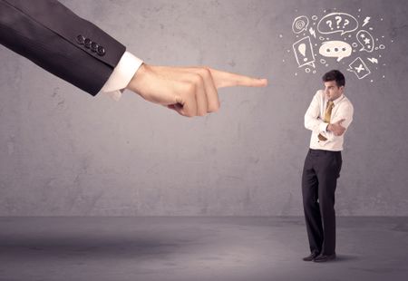 A young confused businessman being fired by large boss hand concept with drawn speech bubbles, exlamation, question marks