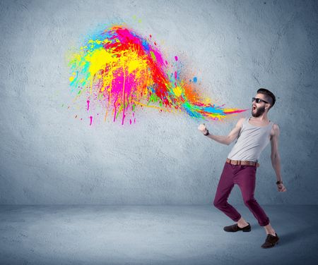 A funny hipster person in casual urban clothing shouting bright colorful paint on city wall concept