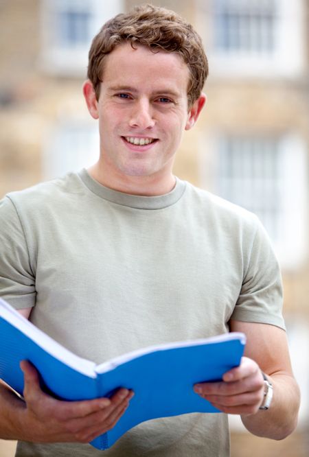 Male student outdoors holding a notebook and smiling