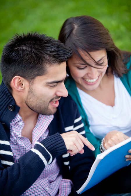 Happy couple of students with a notebook and smiling outdoors