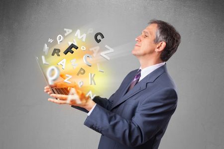 Middle aged businessman in suit holding laptop with colorful letters