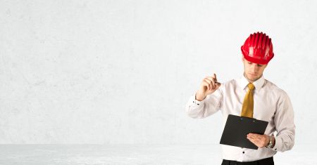 A young architect in red safety helmet planning and drawing with a pen in his hand in empty space in front of a white background.