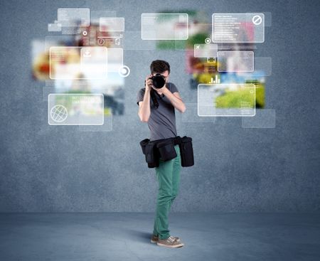 A young professional male photographer holding cameras and taking pictures in front of a blue wall with pictures, icons, text information concept