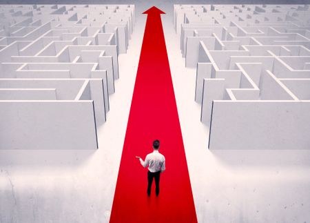 An adult elegant businessman standing on a red carpet arrow pointing ahead through a street with maze on two sides concept