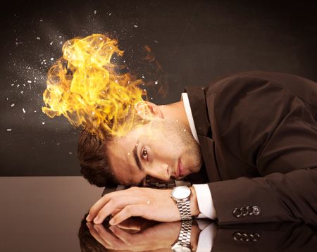 A depressed businessman banging his head in a keyboard and shouting with his head on fire, reflecting on desk