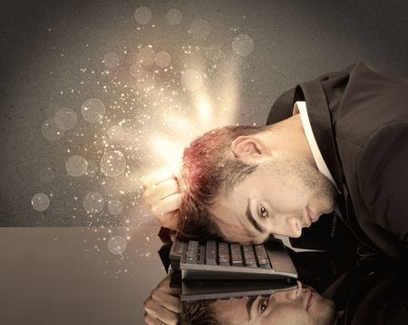 A young depressed business person laying his head on computer keyboard with thoughts exploding from his head illustrated by light beams concept