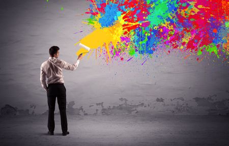 An elegant businessman in suit painting colorful splatter, bright colors on grey urban wall with a paint roller in his hand concept