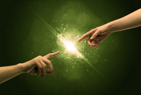 Two naked male hands about to touch, lighting the spark with modest explosion in front of green background concept