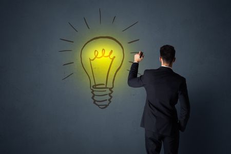 Young businessman in black suit standing in front of a drawn yellow lightbulb 