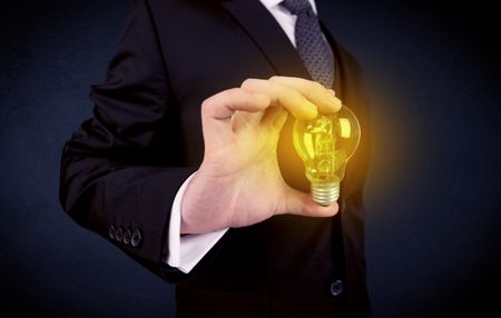 A business man in suit holding a glowing yellow light bulb in his hand while working in the office concept.