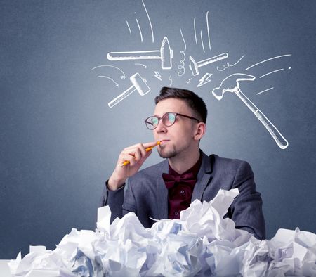 Young businessman sitting behind crumpled paper with drawn hammers hitting his head 