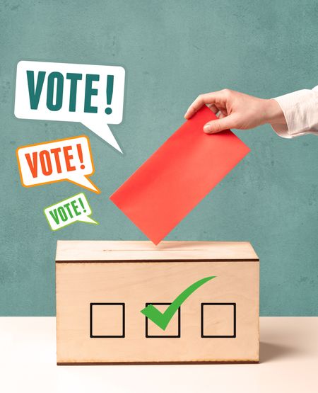 A hand placing a voting slip into a ballot box