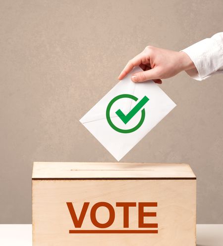 Close up of male hand putting vote into a ballot box, on grunge background