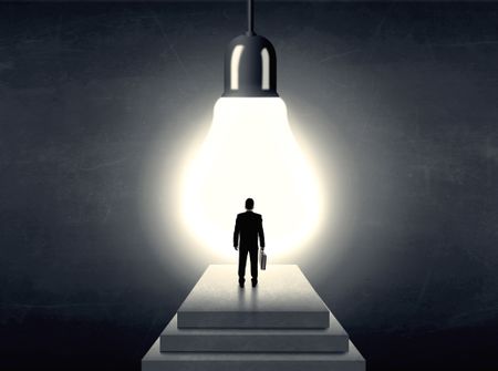 Businessman standing on a step in front of a huge light bulb, concept of having an idea.
