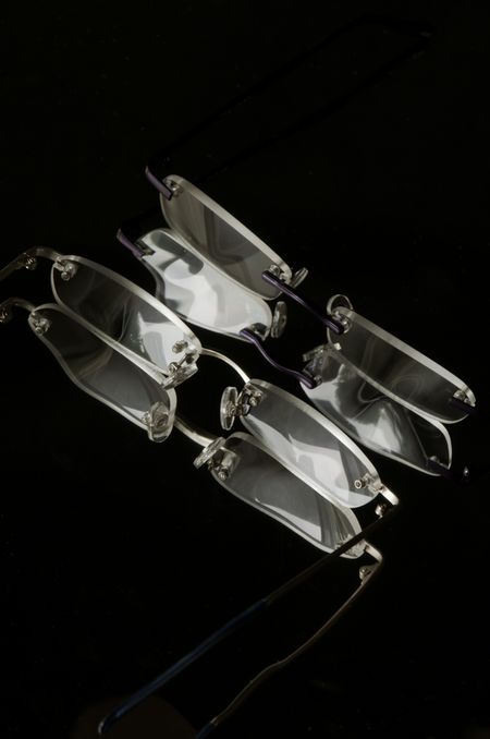 Two pairs of rimless reading glasses facing each other on dark, reflective surface
