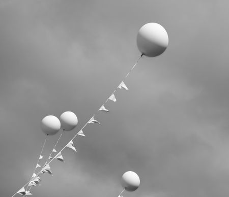 White balloons on long tethers in an overcast sky