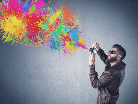 A retro hipster male taking photograph with a vintage camera of an urban wall with paint splatter concept