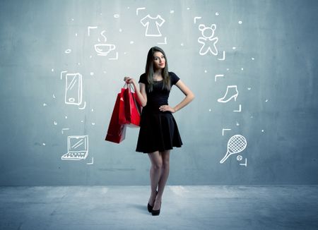 A beautiful young girl in black standing with red shopping bags in front of urban wall background and laptop, shoes, tennis icons concept