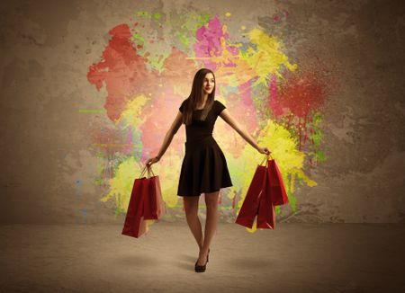 A happy young elegant woman standing with shopping bags in front of brown wall background full of colorful ink splatter concept