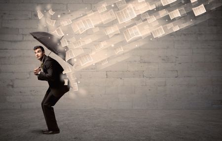 Business man protecting with umbrella against wind of papers concept