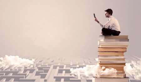 A businessman with laptop tablet in elegant suit sitting on a stack of books on top of sandy labirynth background concept