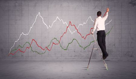 A guy in modern suit standing on a small ladder and drawing a chart on grey wall background with exponential progressing curves, lines