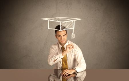 An elegant, successful university student drawing himself a square academic mortarboard cap with a chalk in front of grey wall background concept