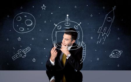 A young happy businessman in elegant suit drawing helmet, satellite and rocket in empty space with a chalk illustration concept