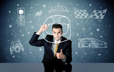 A happy businessman sitting at desk and drawing race car, flag, helmet around himself with a white chalk concept
