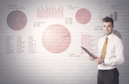 Young sales business male in elegant suit standing in front of brick wall background with lines and pie charts concept