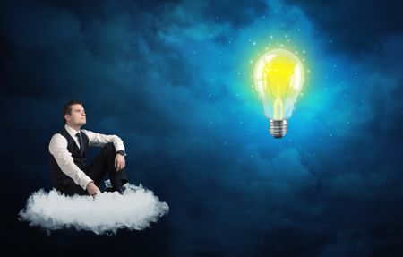 Caucasian businessman sitting on a white fluffy cloud lookind and wondering at a big, shiny, glowing yellow lightbulb