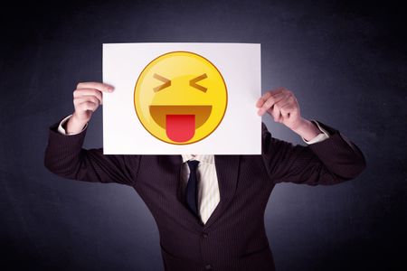 Young businessman hiding behind a playful emoticon on cardboard