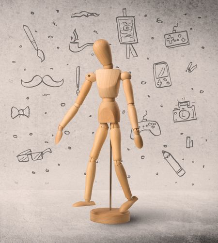 Wooden mannequin posed in front of a greyish background with hobby related scribbles behind it