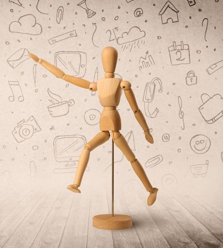 Wooden mannequin posed in front of a greyish background with mixed media scribbles behind it