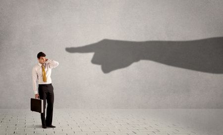Business person looking at huge shadow hand pointing at him concept on background