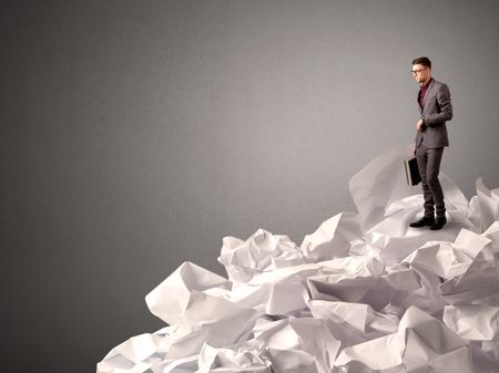 Thoughtful young businessman standing on a pile of crumpled paper with a deep grey background